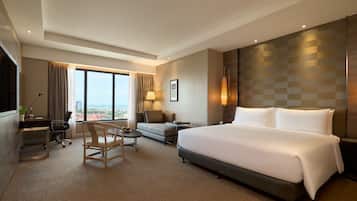 Habitación de hotel con una cama grande, un escritorio, una silla, un sofá y vistas a la ciudad.