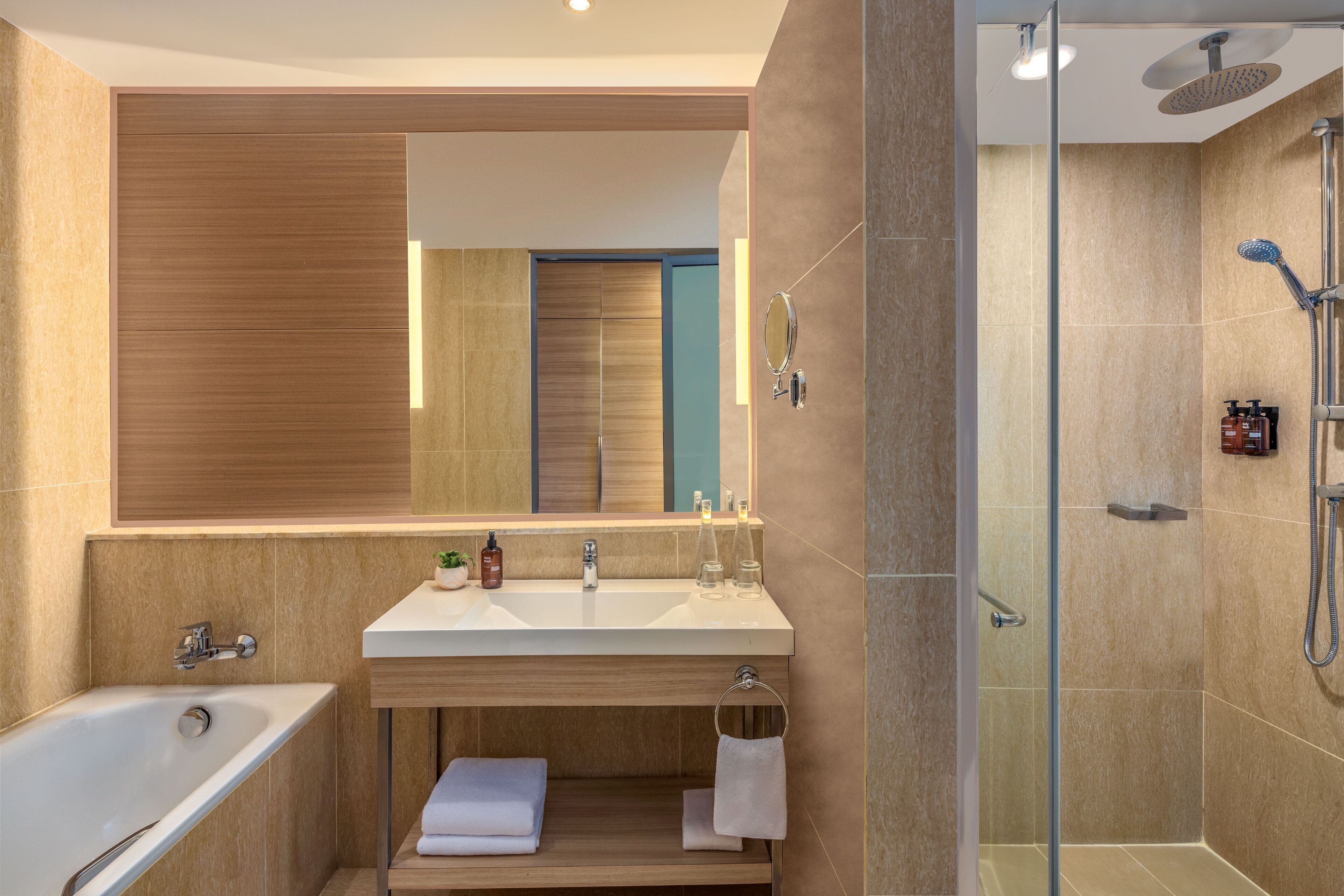 A modern bathroom with a large mirror, a bathtub, a shower, and a vanity with a sink and countertop.