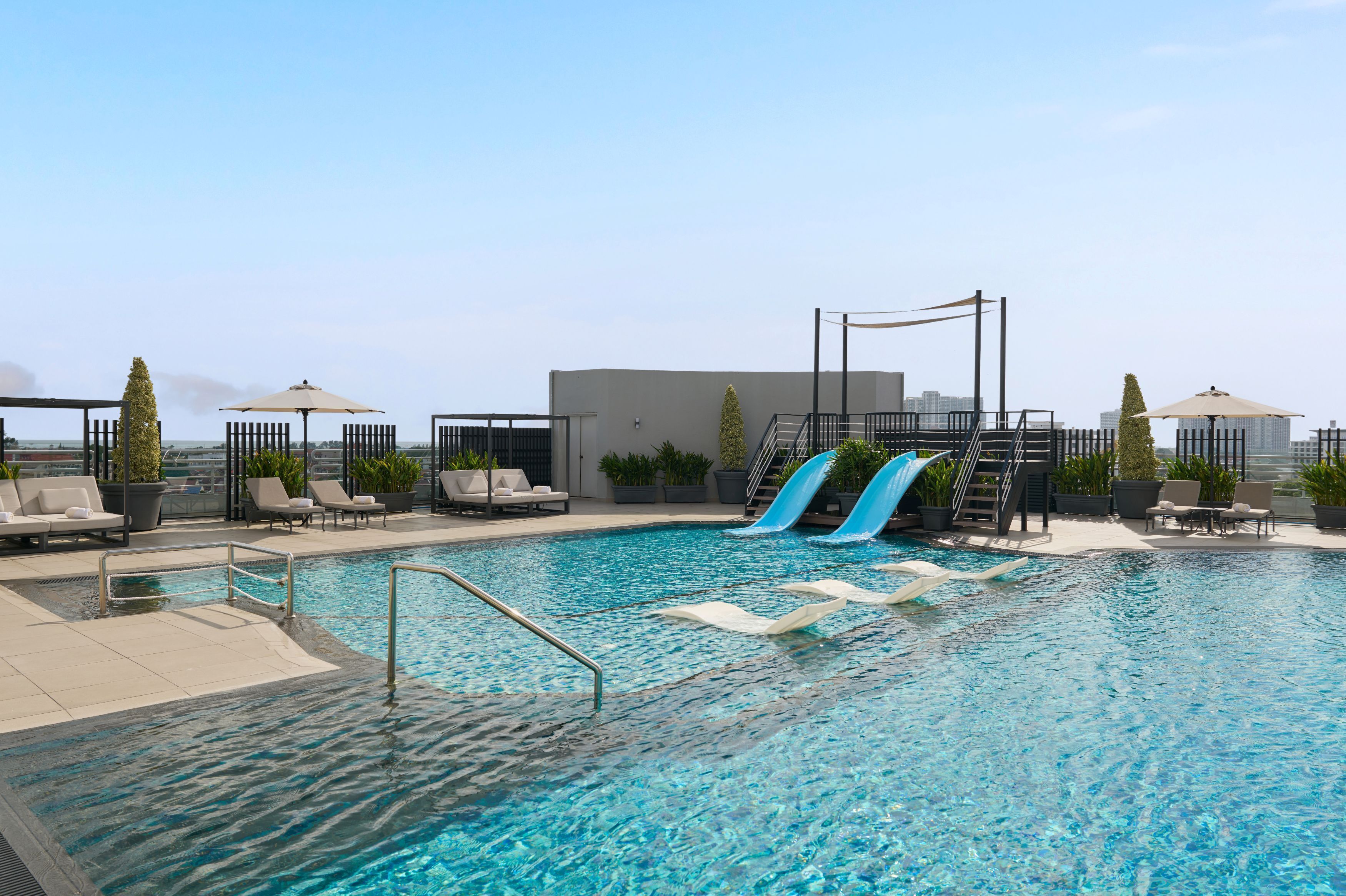 A rooftop pool with slides, lounge chairs, and potted plants.