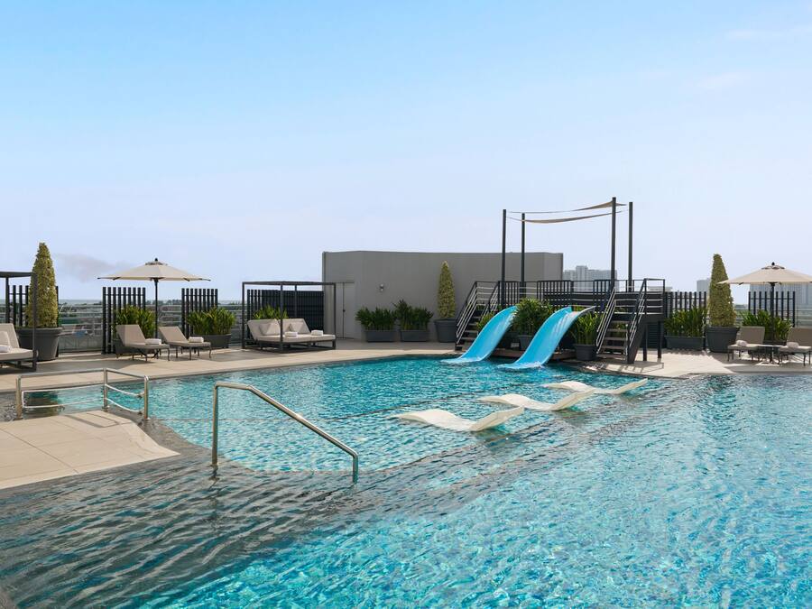 A rooftop pool with slides, lounge chairs, and potted plants.