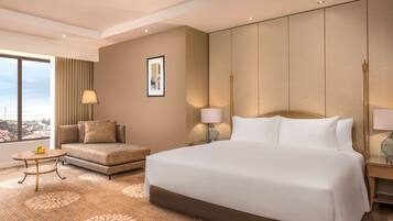 Quarto de hotel com uma cama grande, um sofá, uma mesinha e vista para a cidade.
