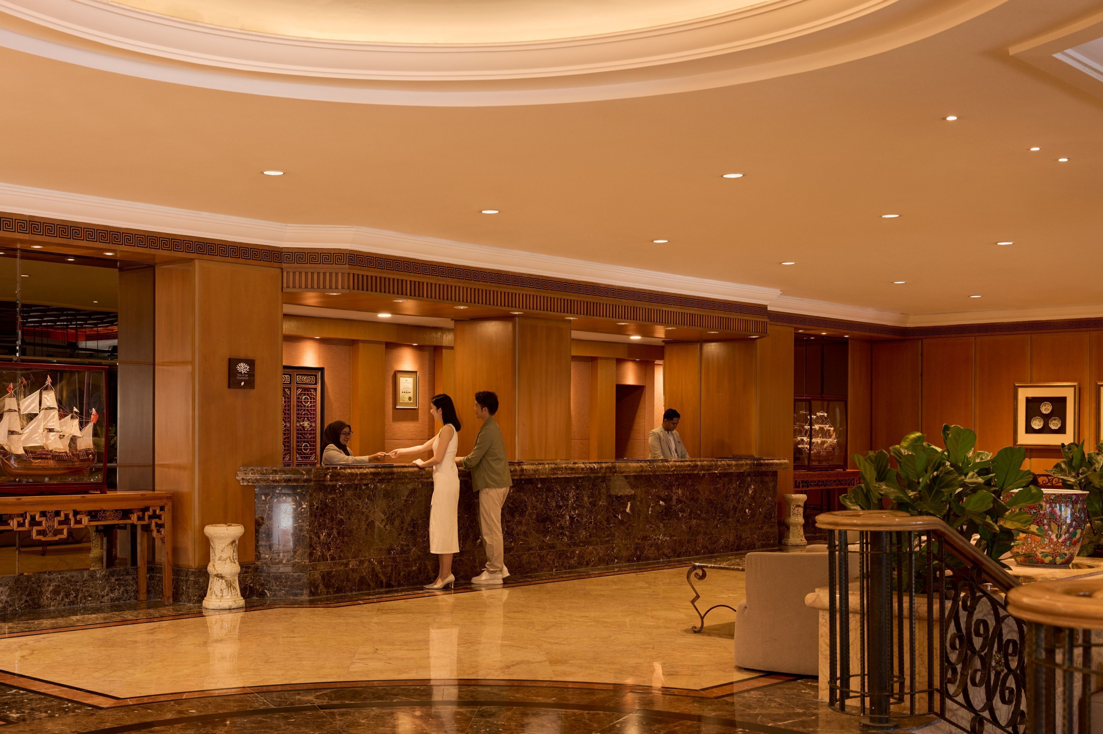 Vestíbulo de hotel con mostrador de recepción, suelo de mármol y una maqueta decorativa de barco.