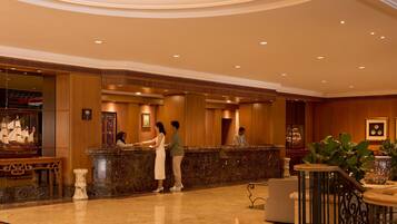 Vestíbulo de hotel con mostrador de recepción, suelo de mármol y una maqueta decorativa de barco.