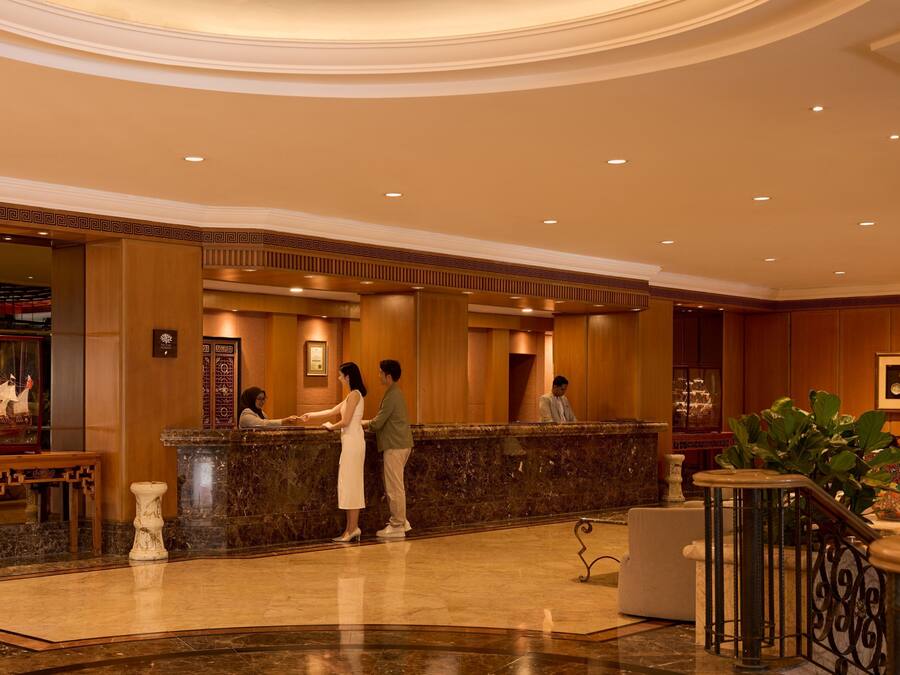 A hotel lobby with a reception desk, marble flooring, and a decorative ship model.