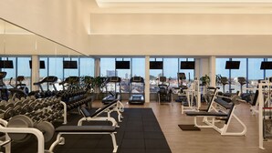 Ein Fitnessstudio mit Cardiogeräten, Krafttrainingsgeräten und großen Fenstern mit Blick auf die Stadt.