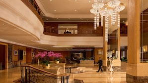 Eine mehrstöckige Lobby mit Marmorboden, einem beeindruckenden Chandelier und einer Rezeption.