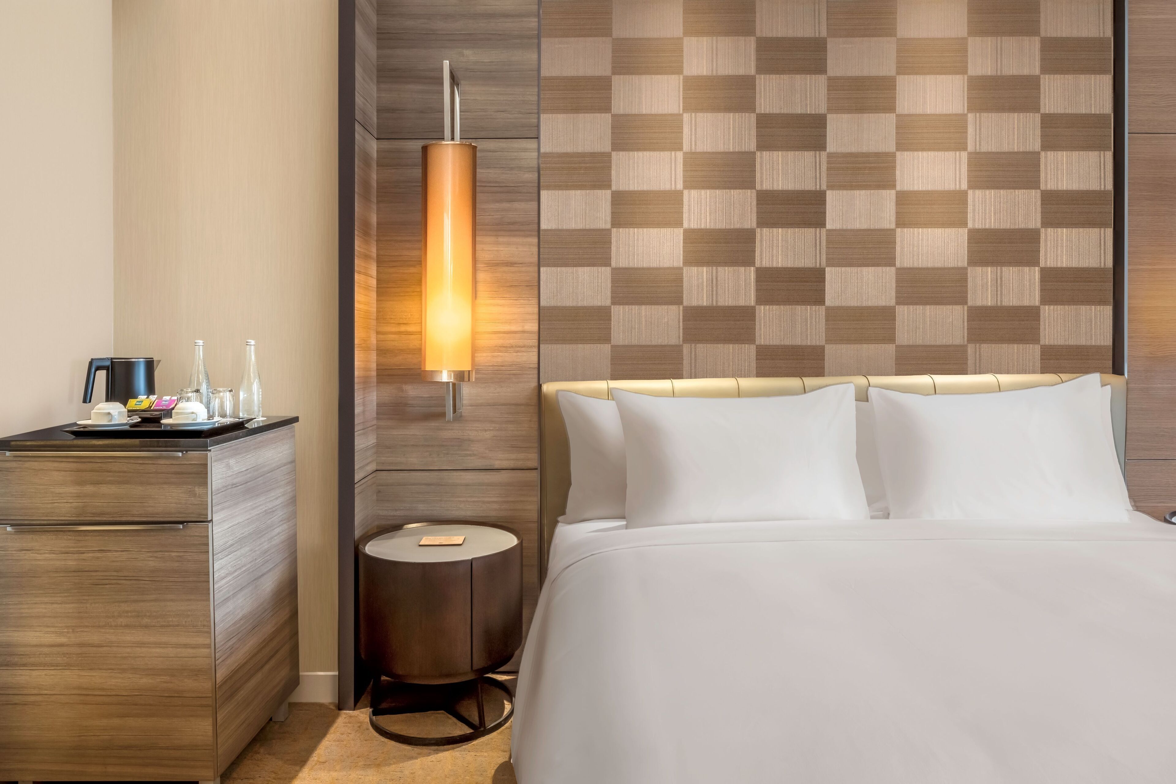 A hotel room with a bed, bedside table, lamp, and a wall with a checkered pattern.