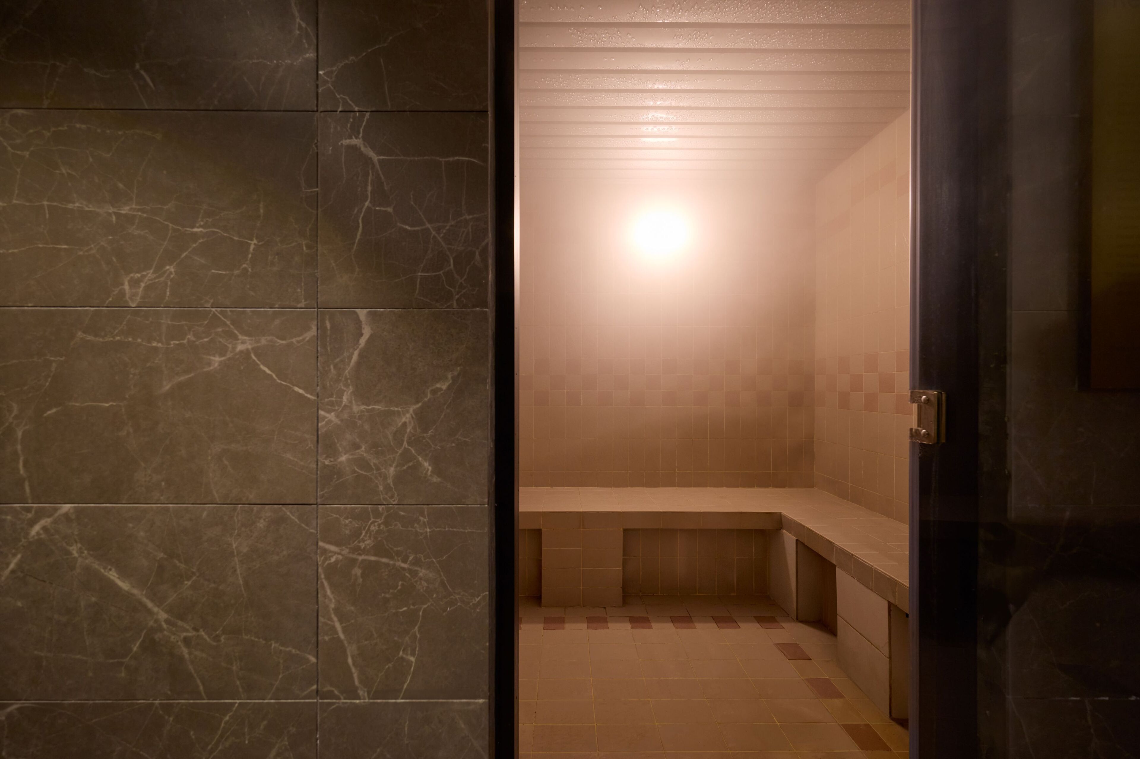 A bathroom with marble walls, a bench, and a tiled floor.