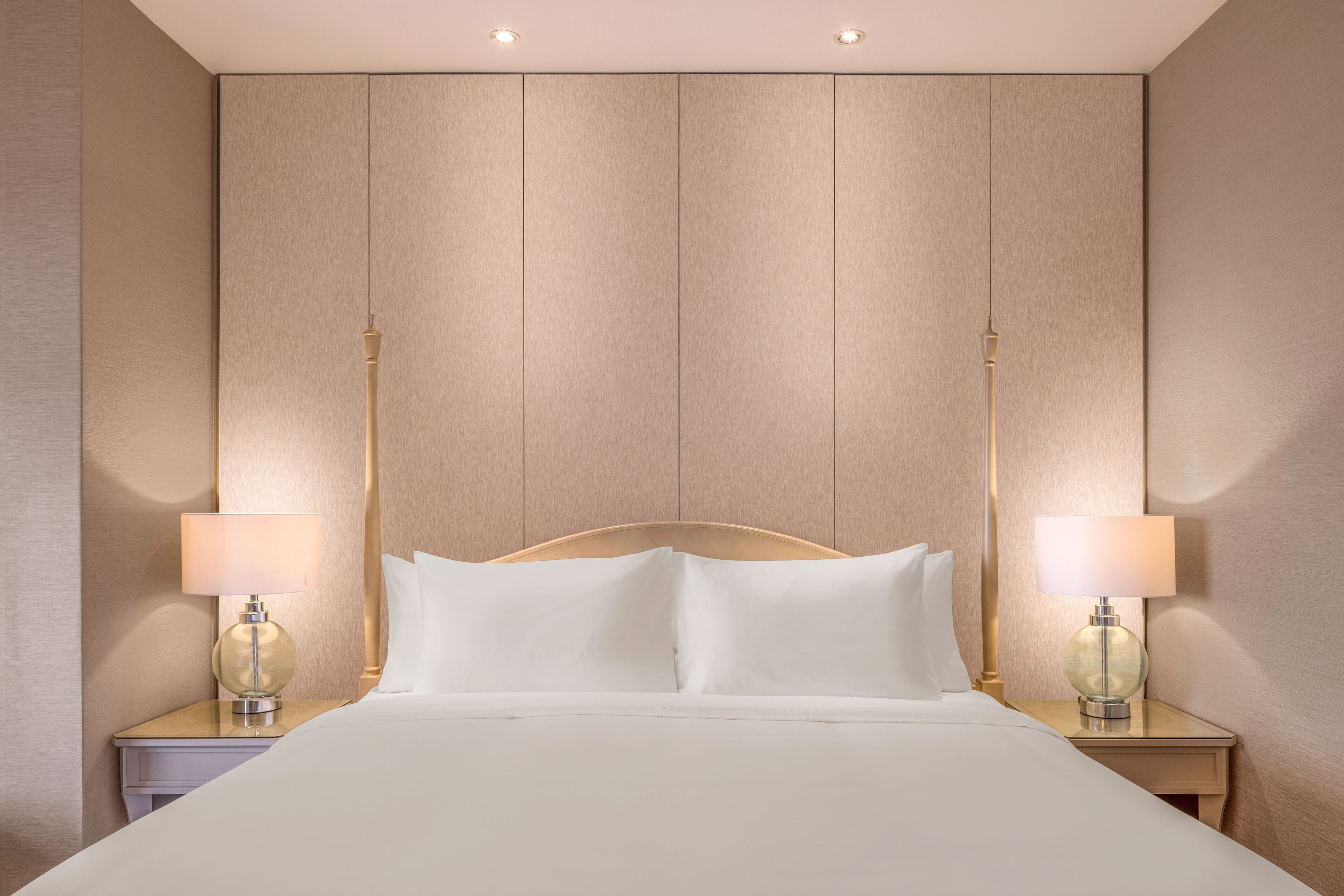 Una habitación de hotel con una cama grande, dos mesitas de noche con lámparas y un cabecero de madera.