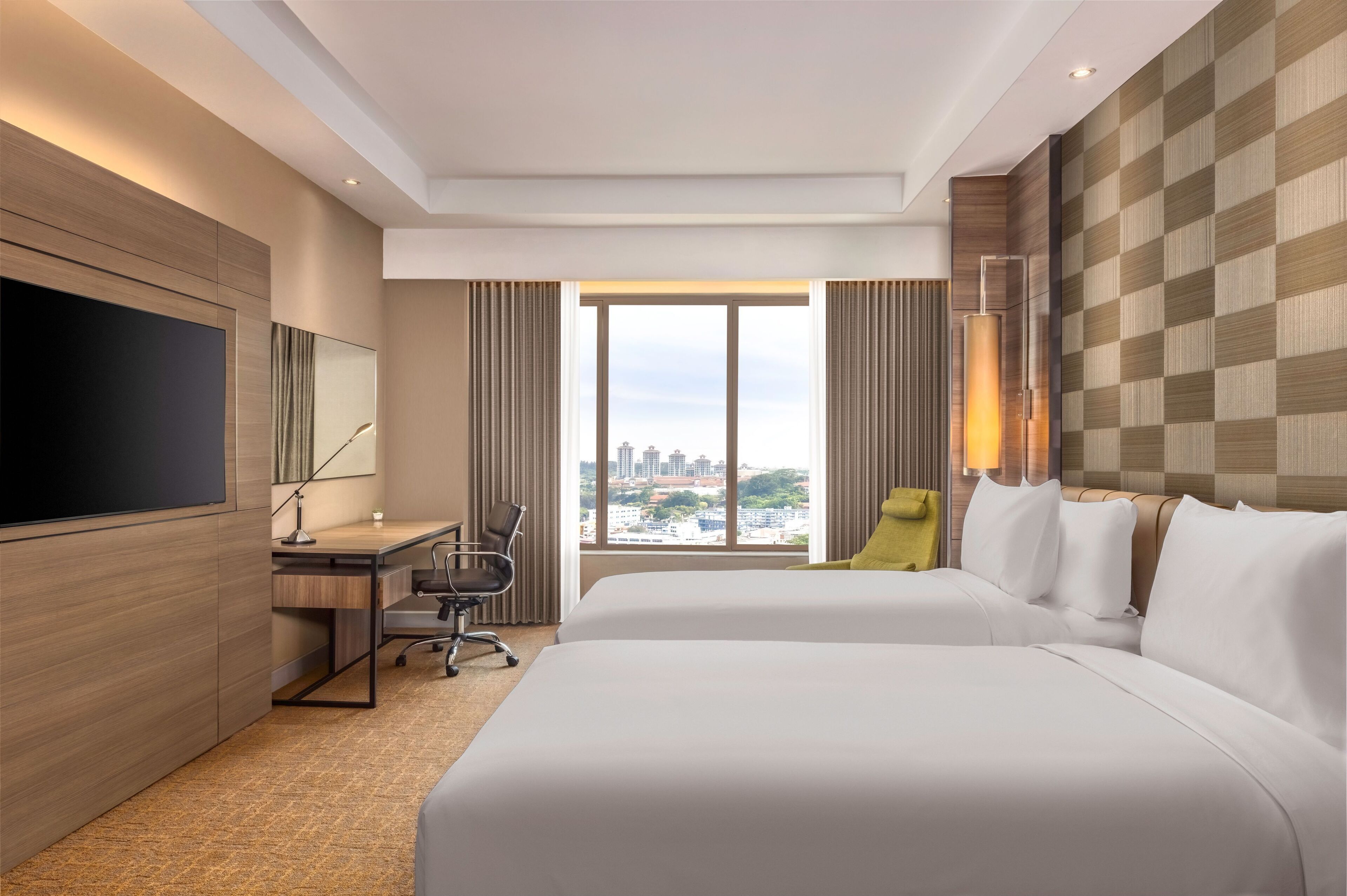 Quarto de hotel com uma cama grande, uma escrivaninha, uma cadeira, uma televisão e vista para a cidade pela janela.