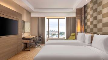 Quarto de hotel com uma cama grande, uma escrivaninha, uma cadeira, uma televisão e vista para a cidade pela janela.