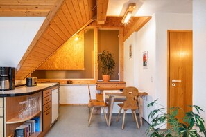 A kitchen with wooden cabinets, a dining table, chairs, a coffee maker, and a potted plant. - Holiday Apartment '2' with Shared Garden and Wi-Fi (Müllheim im Markgräflerland)