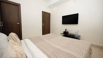 A bedroom with a bed, a TV mounted on the wall, and a door.