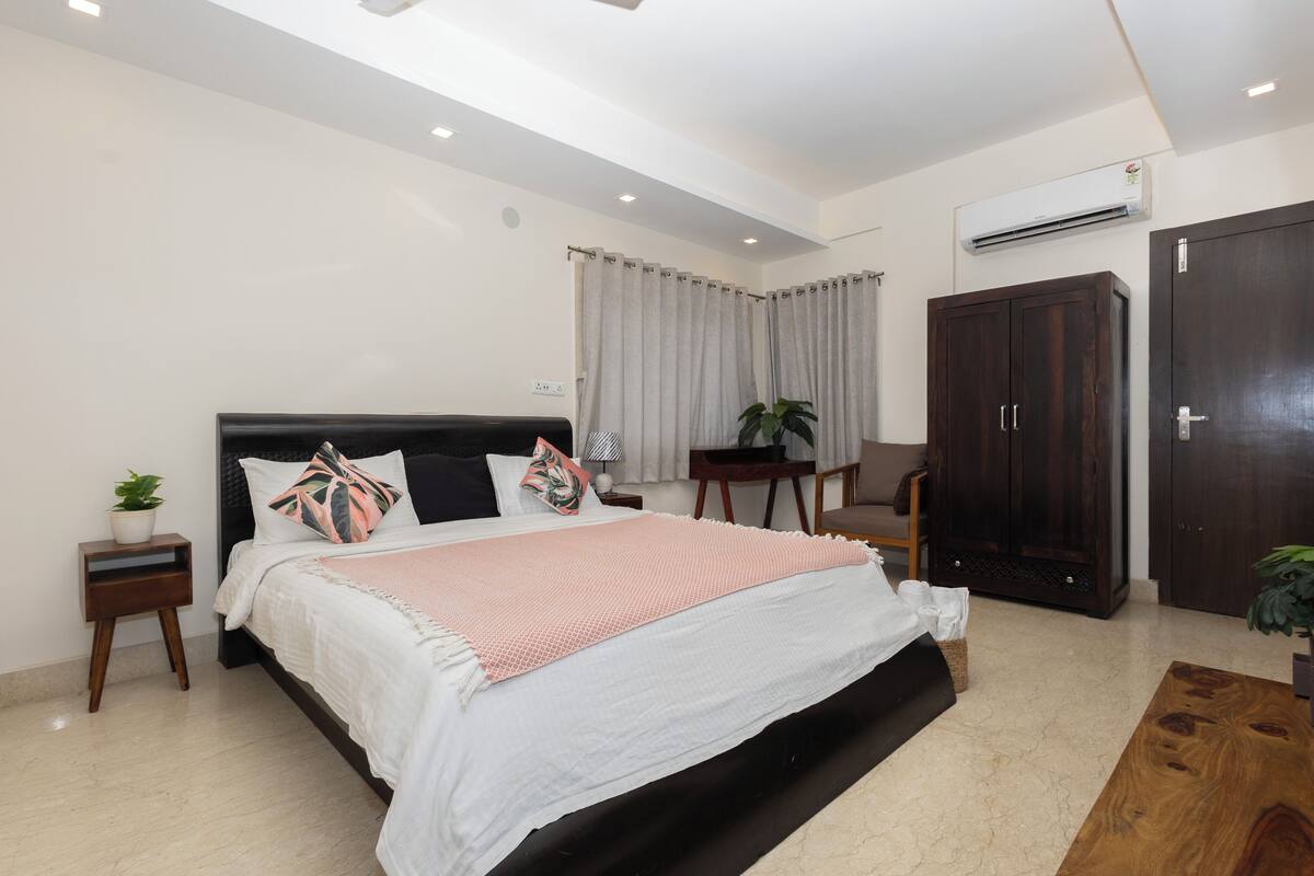 A bedroom with a large bed, a bedside table with a lamp, a wardrobe, and a small table with a chair.