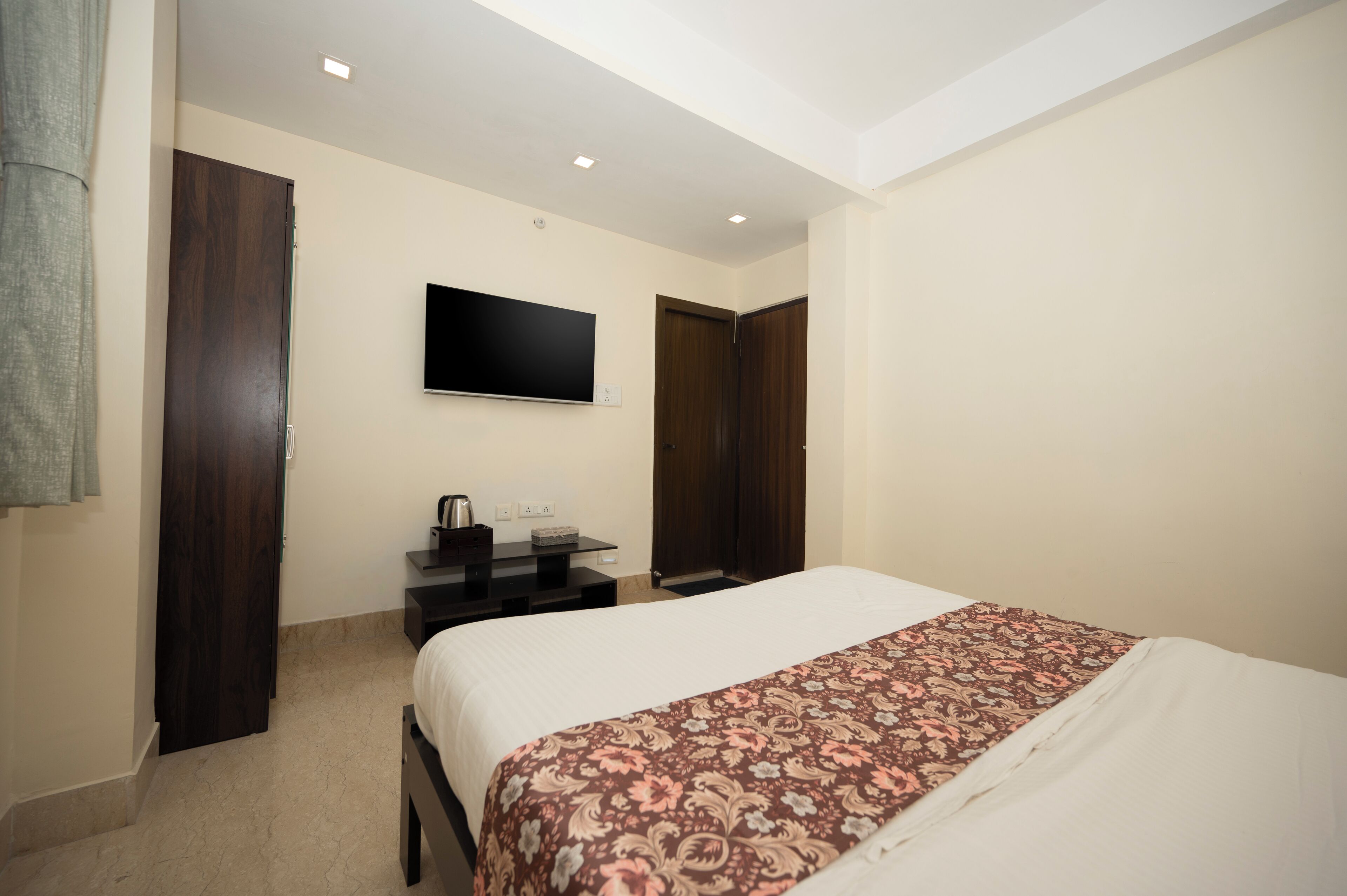 Een hotelkamer met een bed, een flatscreen-tv aan de muur, een bureau met een koffiezetapparaat en een kledingkast.