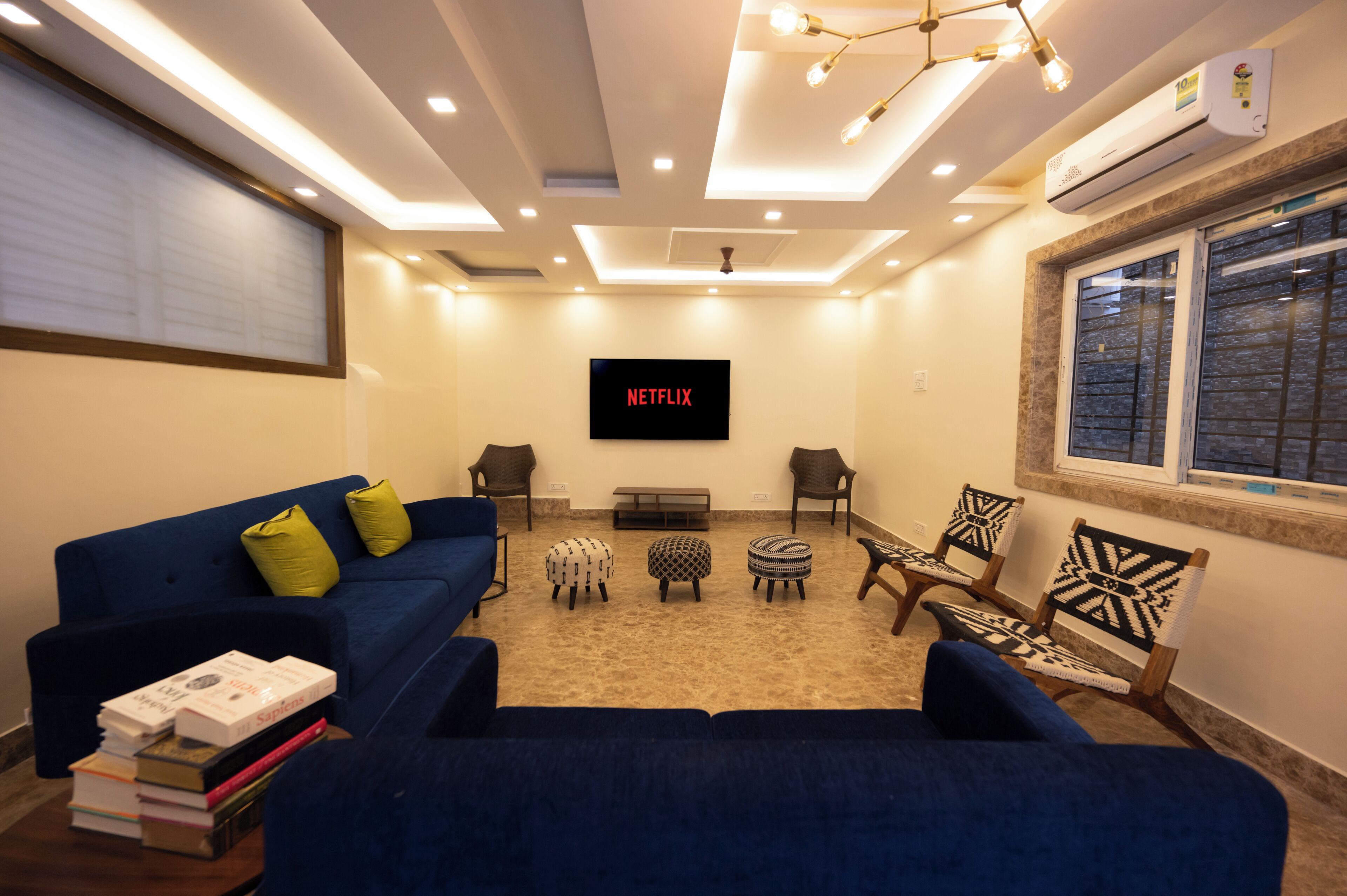 A living room with a blue sofa, two armchairs, a coffee table, and a TV mounted on the wall displaying 'NETFLIX'.