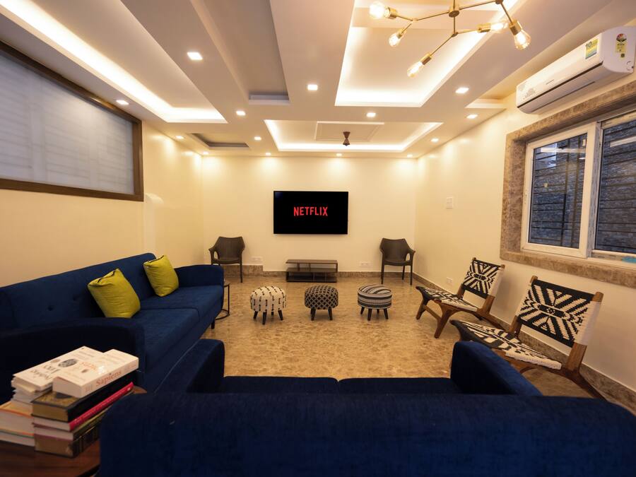 A living room with a blue sofa, two armchairs, a coffee table, and a TV mounted on the wall displaying 'NETFLIX'.