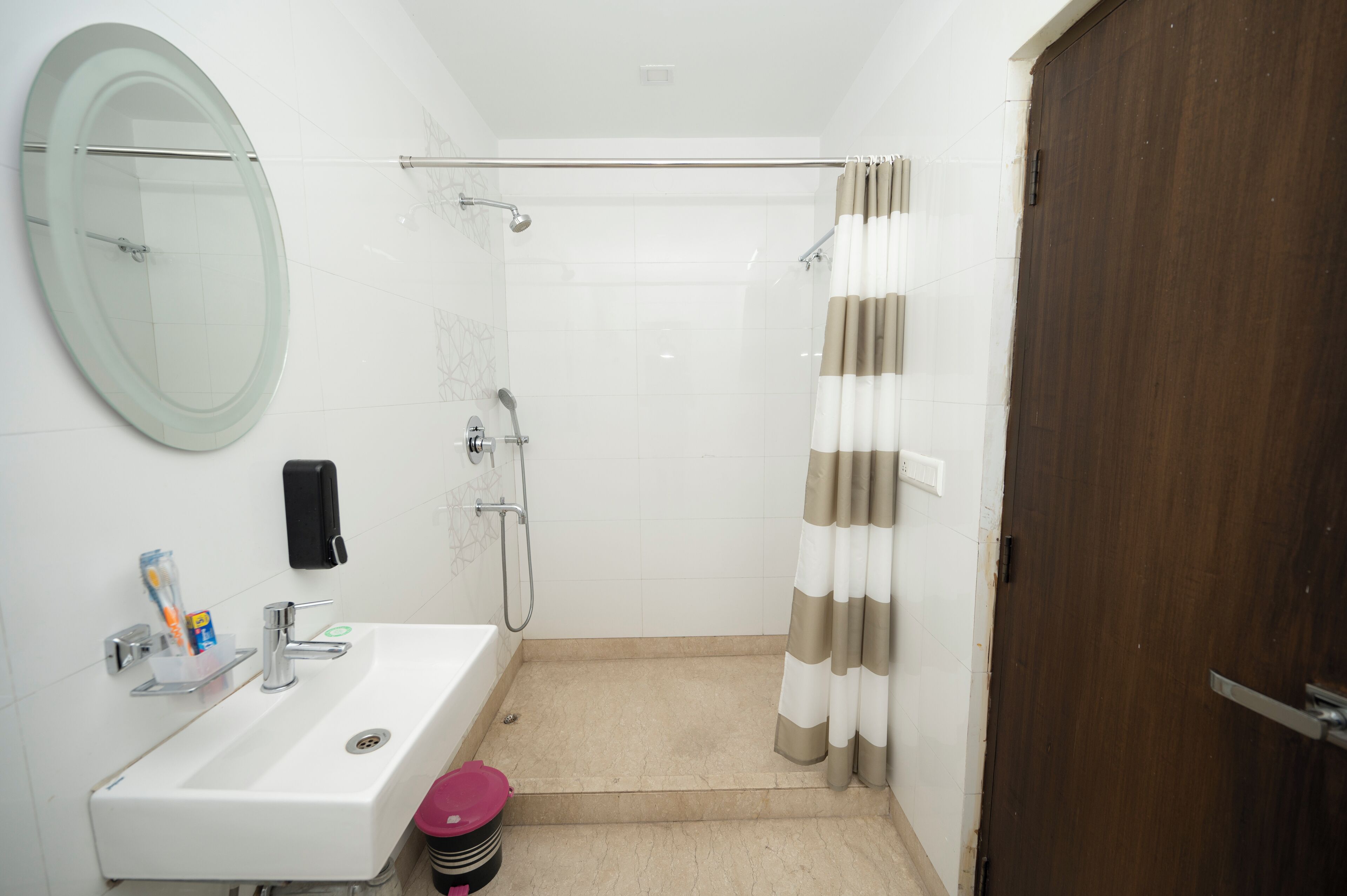 A bathroom with a sink, mirror, shower, and a wooden door.
