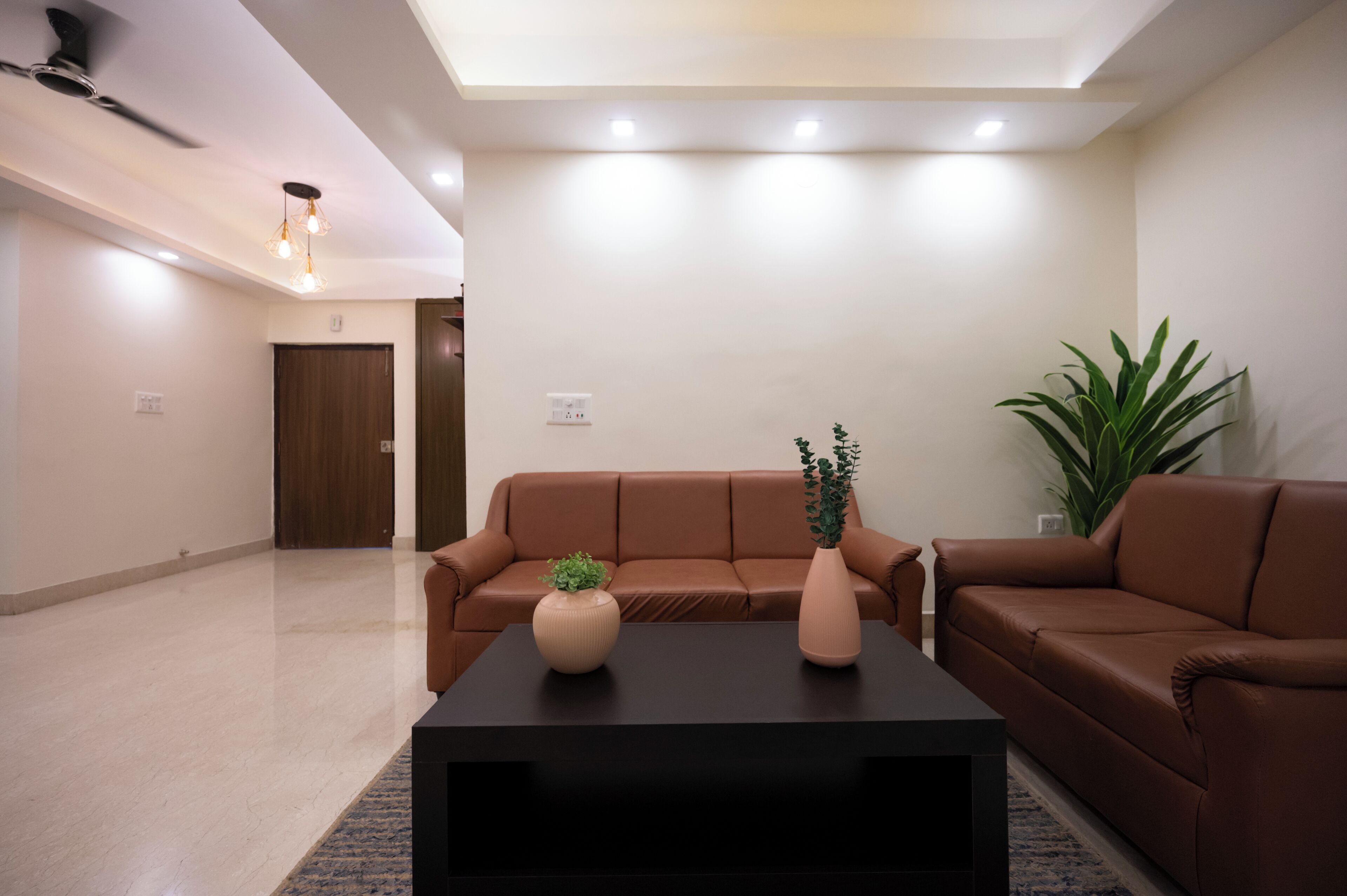 Una sala de estar moderna con un sofá de cuero marrón, una mesa de centro negra y dos jarrones con plantas.