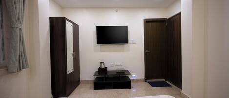 A hotel room with a bed, a flat-screen TV mounted on the wall, a small table with a kettle, and a wardrobe.