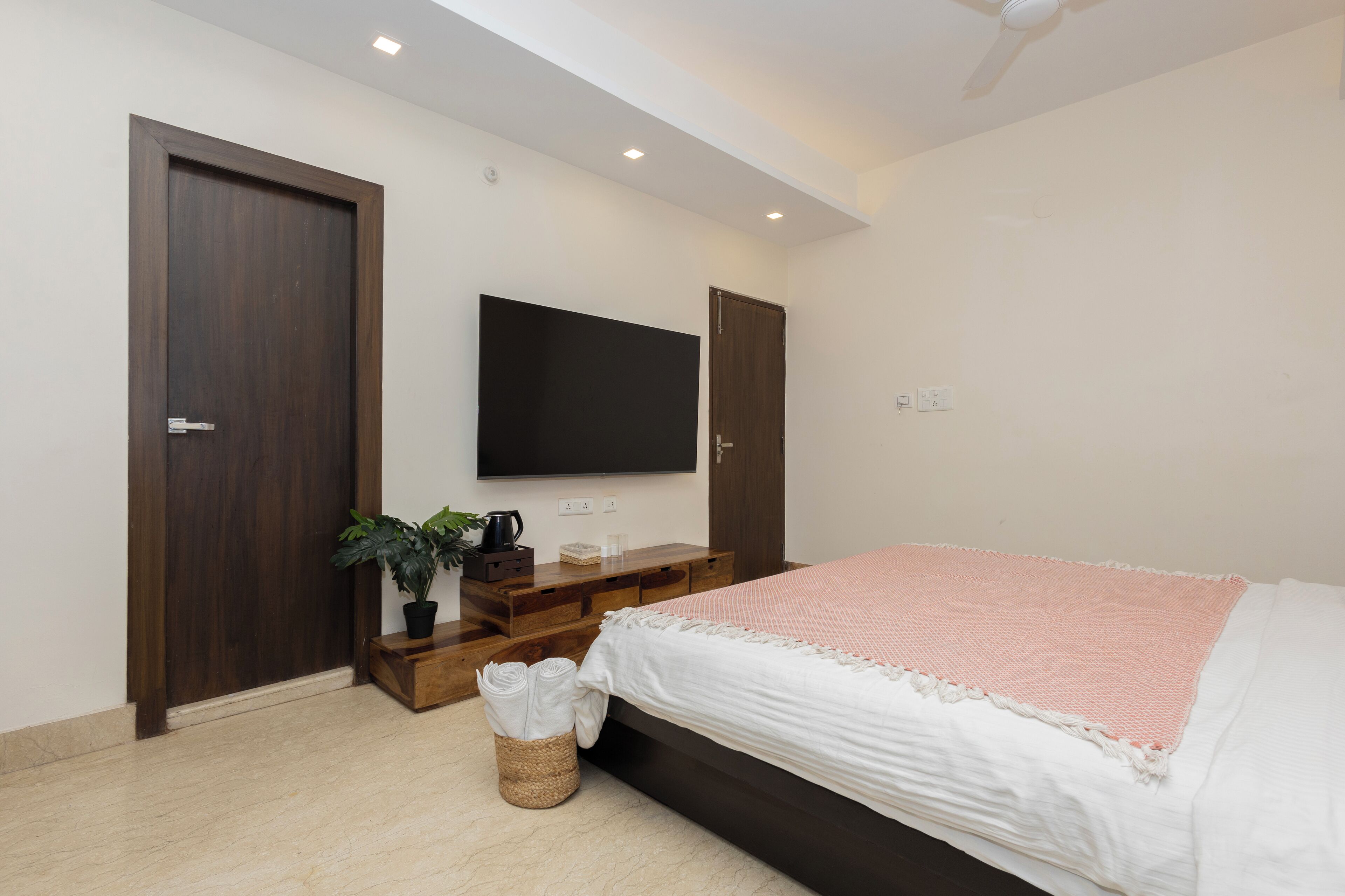 A bedroom with a bed, a TV mounted on the wall, and a wooden wardrobe.