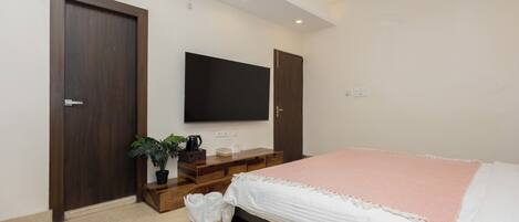 A bedroom with a bed, a TV mounted on the wall, and a wooden wardrobe.