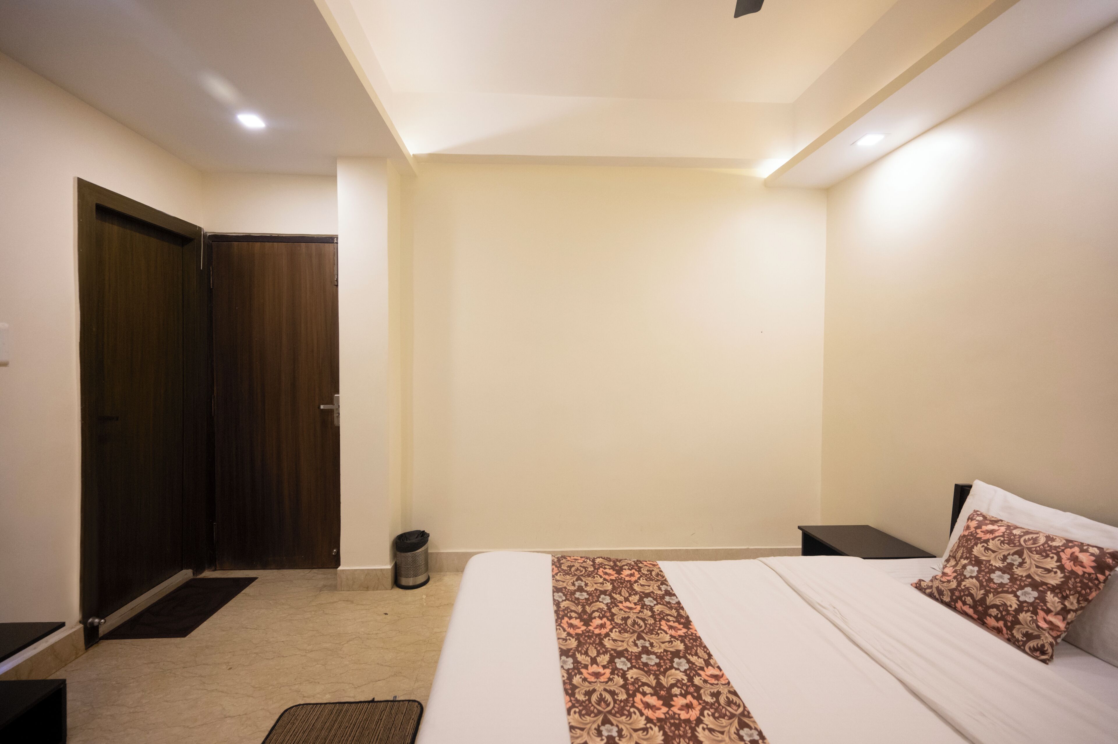 Una habitación de hotel con una cama, una mesita de noche, un cesto de basura y una puerta.