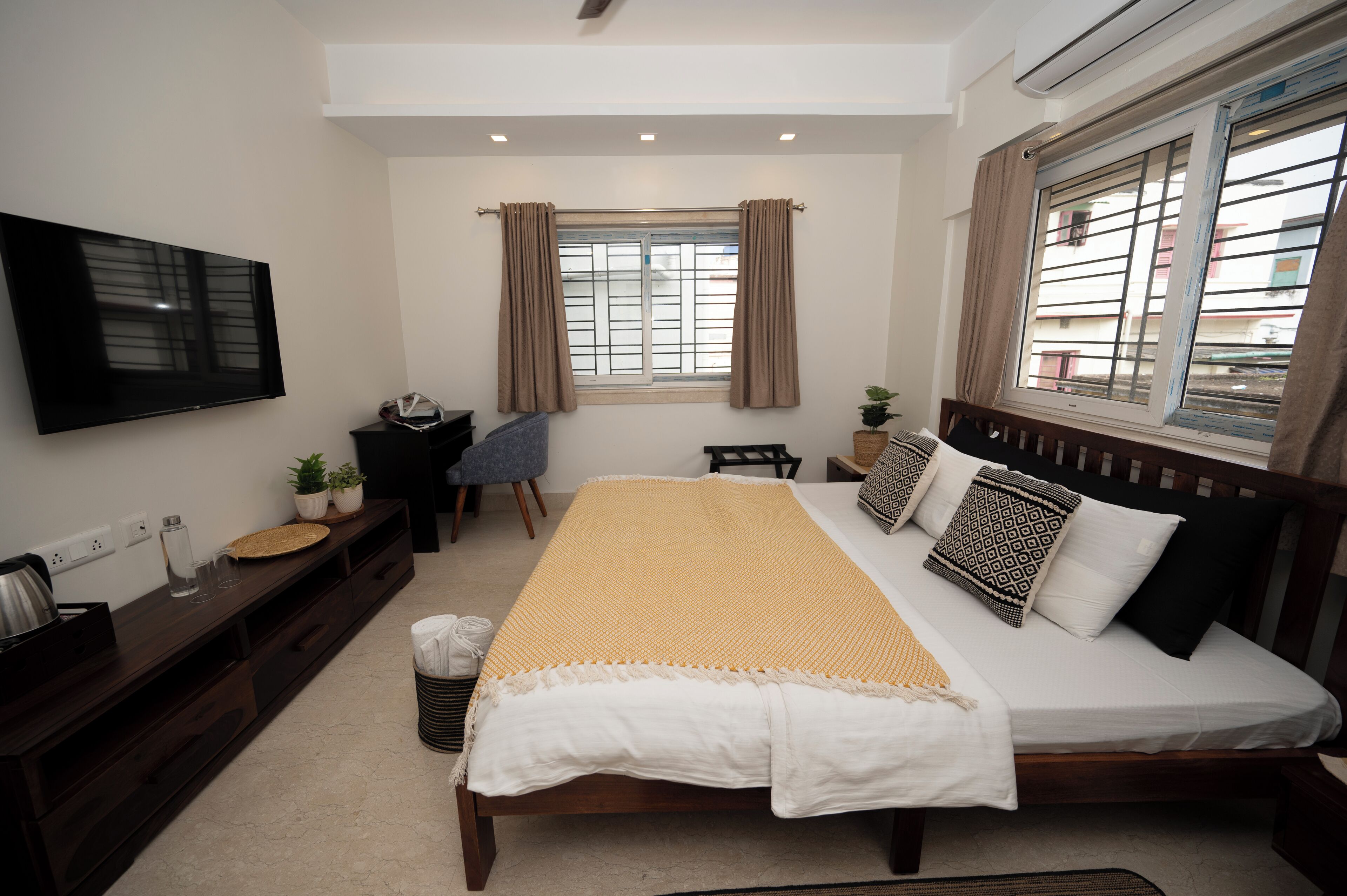 A bedroom with a bed, a desk, a chair, a TV, and a window with curtains.