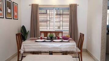 A dining area with a table set for four, a window with curtains, and framed artwork on the wall.