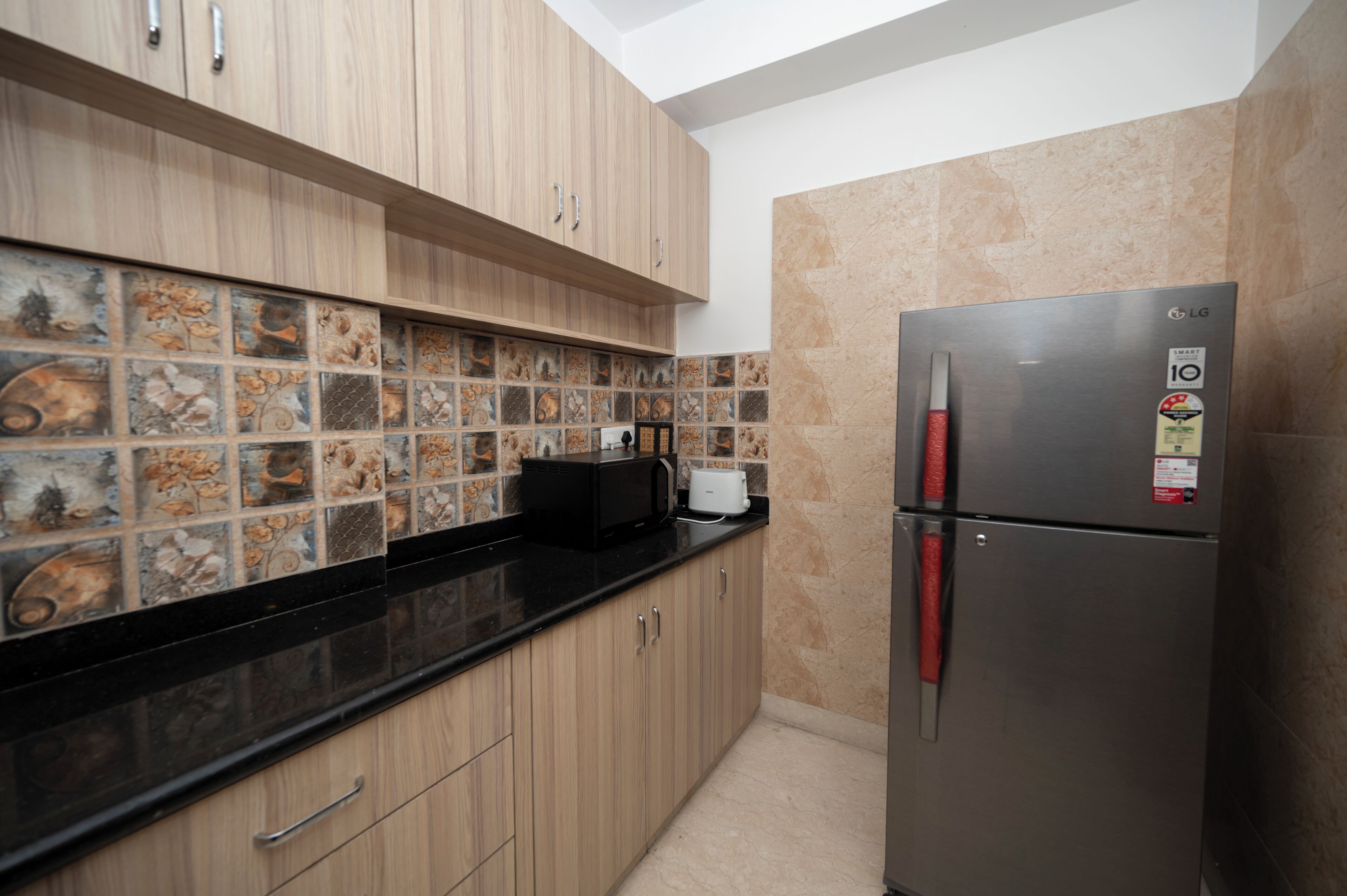 A compact kitchen with wooden cabinets, a black countertop, a stainless steel refrigerator, and decorative tile backsplash.