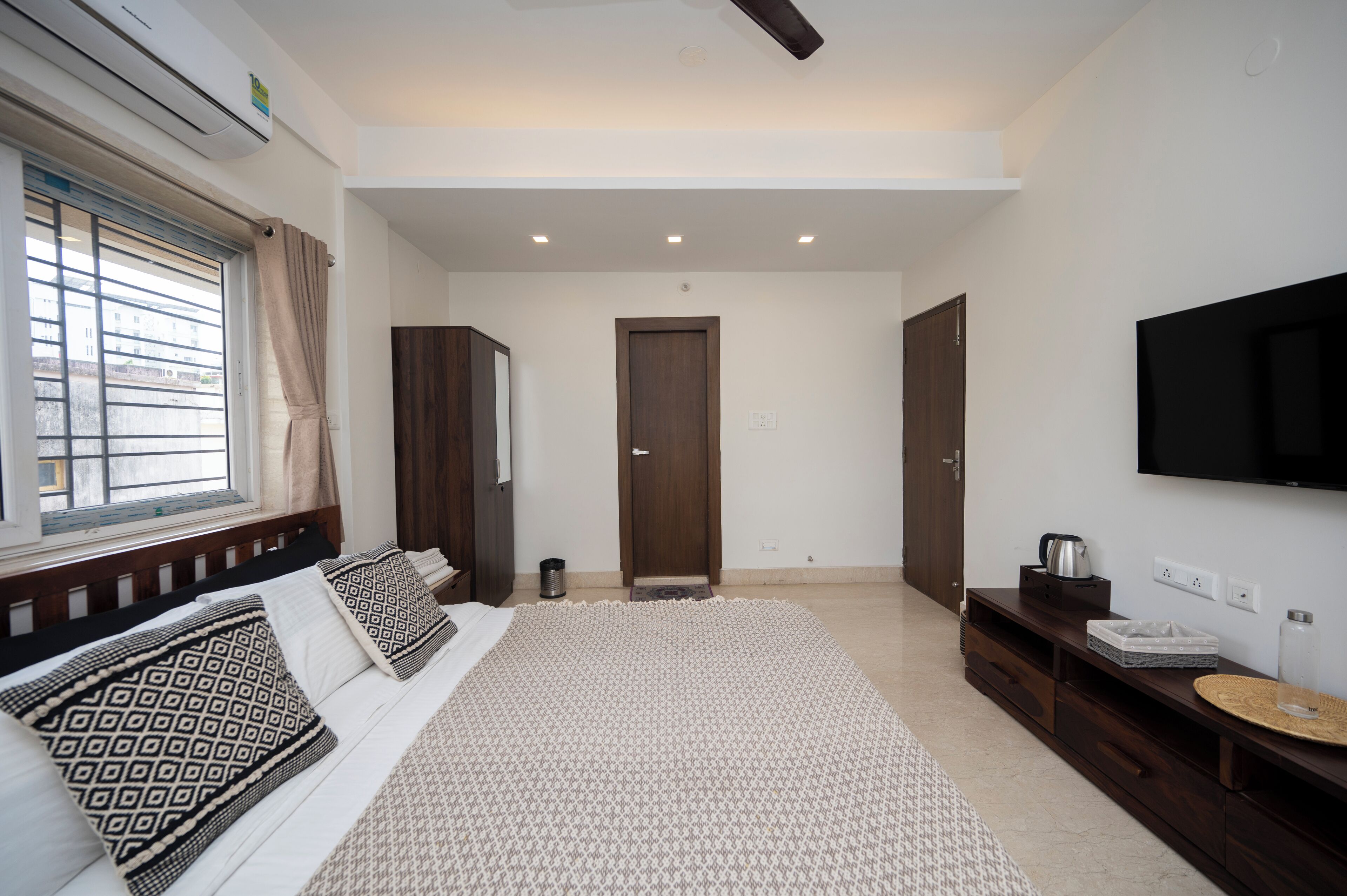 A modern bedroom with a large bed, a TV mounted on the wall, and a window with curtains.