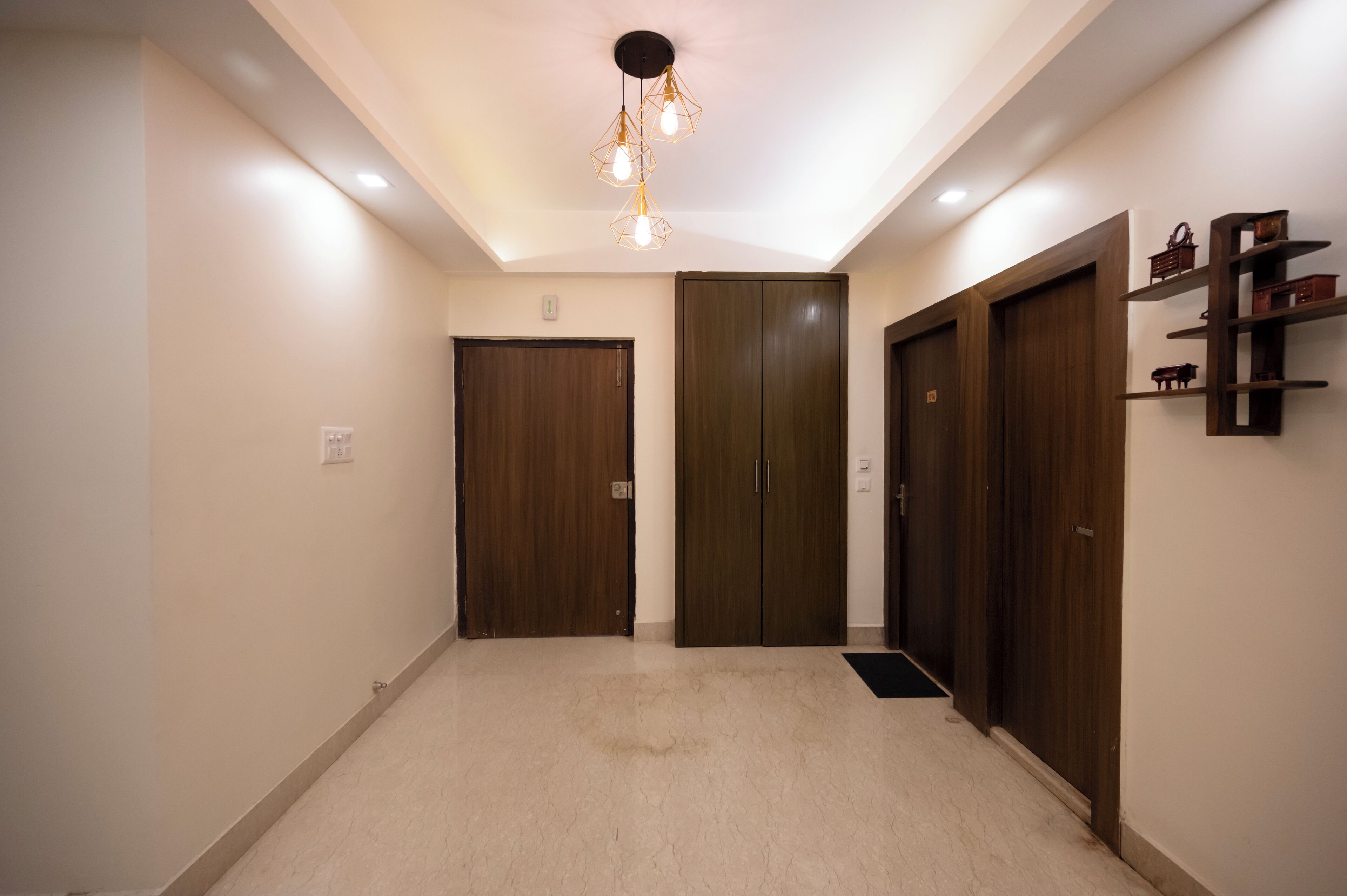 A hallway with a light fixture, wooden doors, and a wall-mounted shelf.