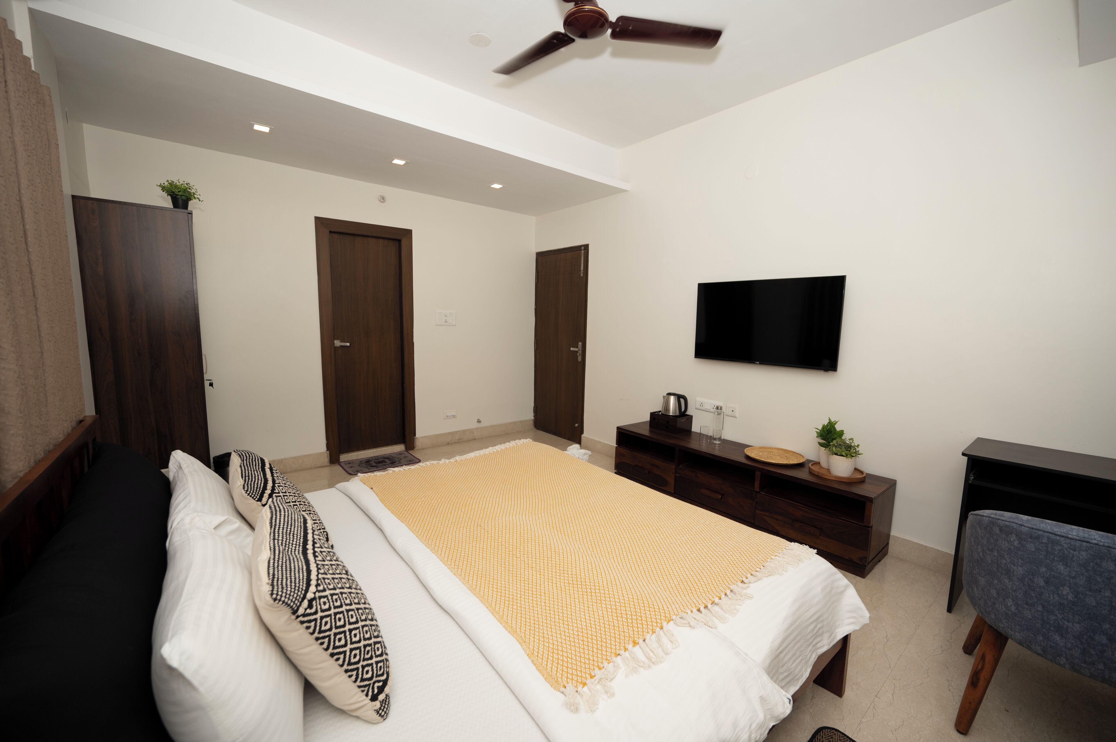 A modern bedroom with a bed, a desk, a television, and a ceiling fan.