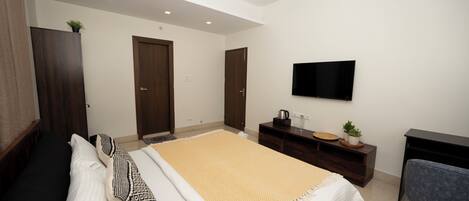 A modern bedroom with a bed, a desk, a television, and a ceiling fan.