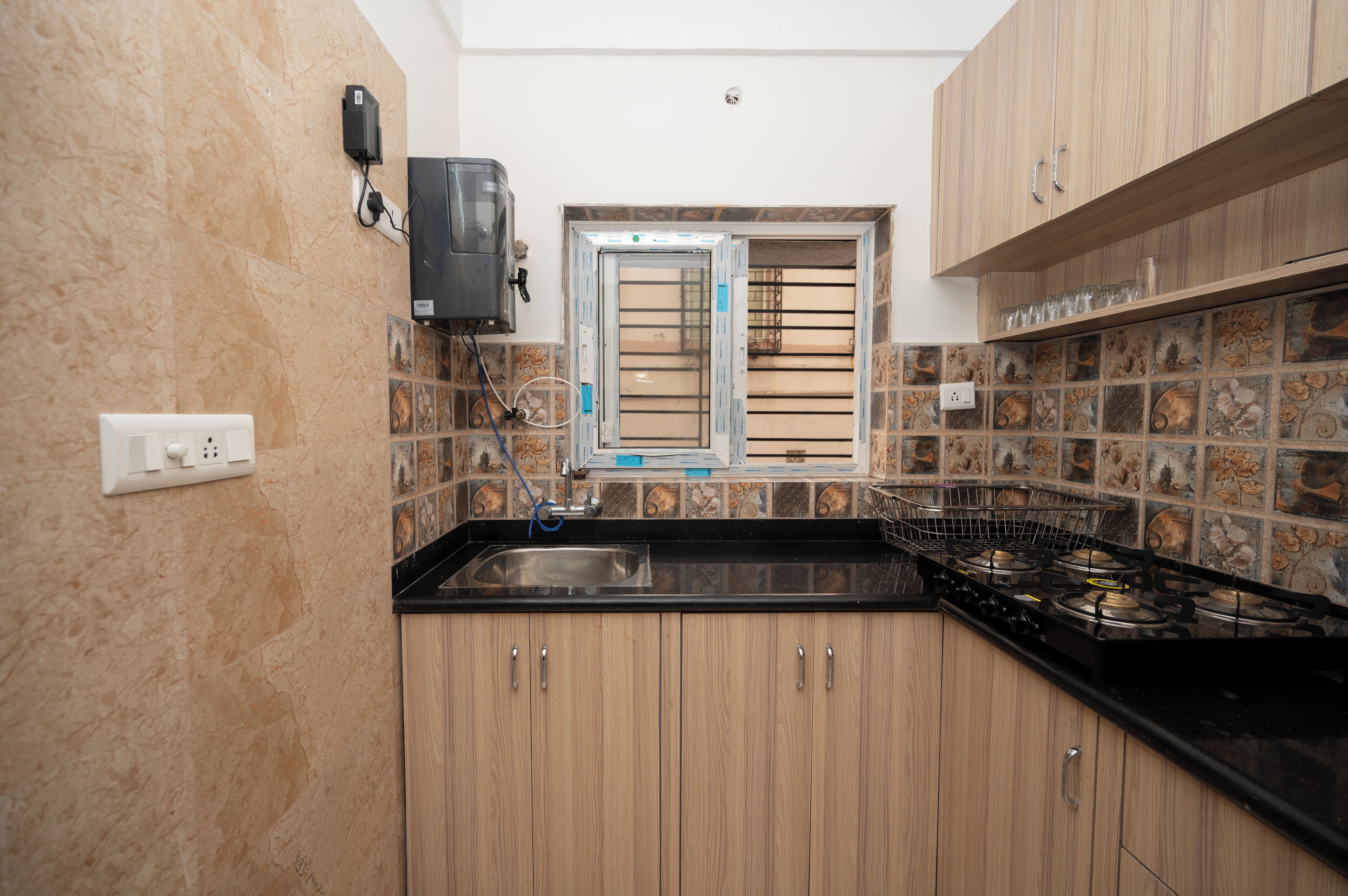 A kitchen with wooden cabinets, a black countertop, a gas stove, a window with blinds, and a tiled backsplash.