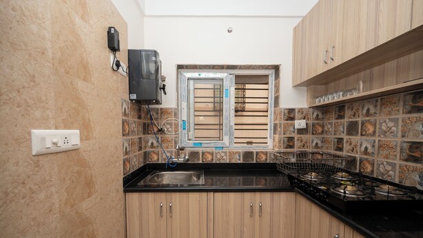 Una cucina con mobili in legno, un piano di lavoro nero, un fornello a gas, una finestra con persiane e uno schienale piastrellato.