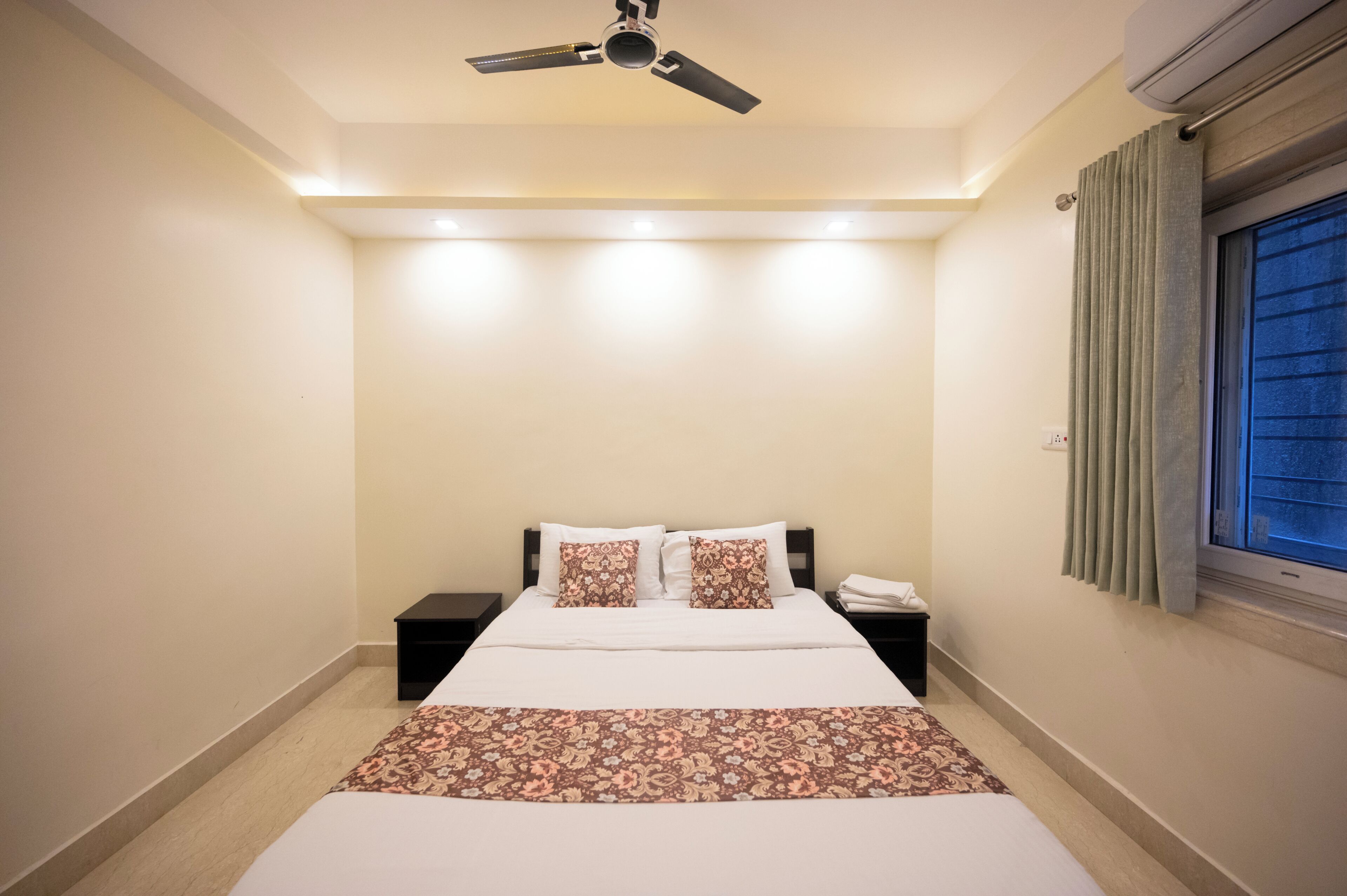 A bedroom with a bed, a nightstand, a ceiling fan, and a window with curtains.