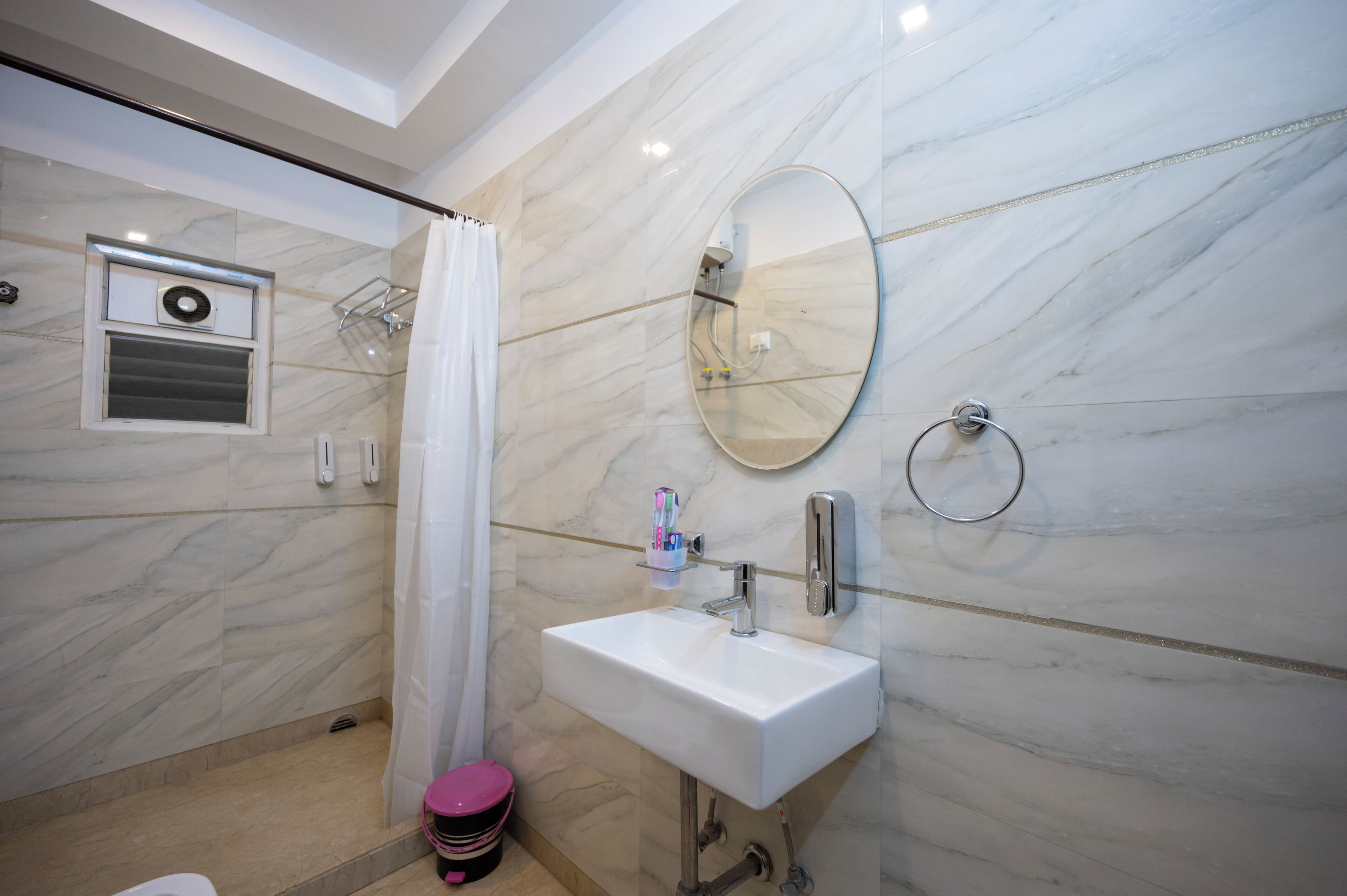A bathroom with a marble wall, a white sink, a mirror, a shower, and a toilet.