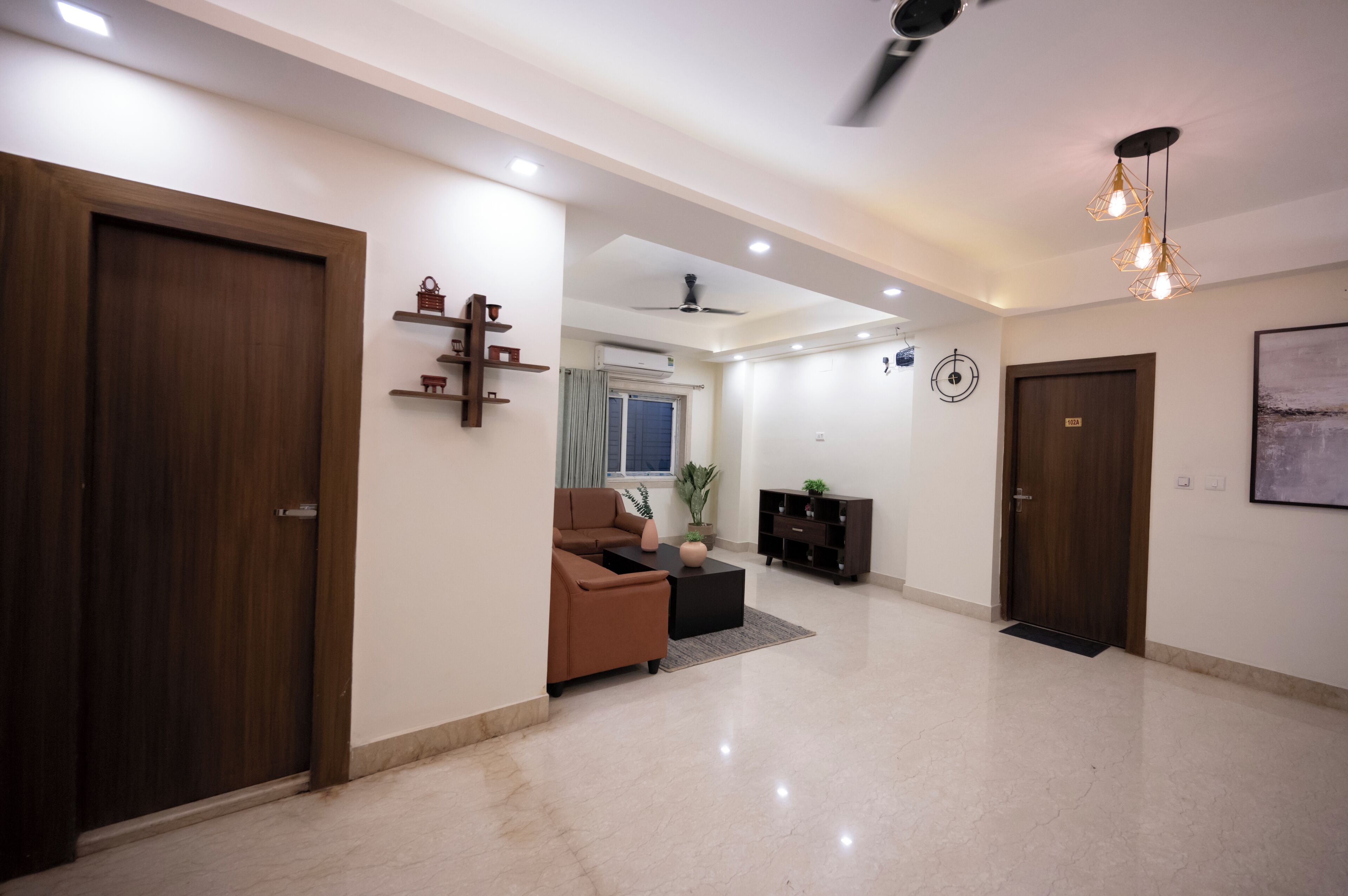 A spacious living area with a sofa, coffee table, and decorative items. There are wooden doors, a ceiling fan, and recessed lighting.