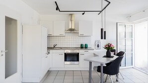 Una cocina moderna con armarios blancos, un horno de acero inoxidable y un comedor con mesa y sillas.