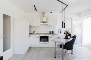 Une cuisine moderne avec des meubles blancs, un four en acier inoxydable et un coin repas comprenant une table et des chaises.