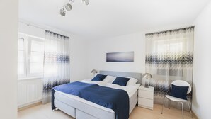 Un dormitorio con cama, mesitas de noche, una silla y ventana.