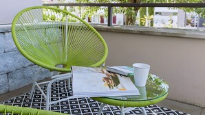 Una silla verde y una mesa con una revista y una taza blanca encima, frente a una pared con piso estampado.