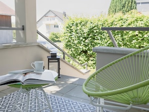 A balcony with a green chair, a small table with a book and a cup, and a staircase leading to a house. - Holiday Apartment 'Im Fischerhaus' with Private Terrace and Wi-Fi (Nonnenhorn)