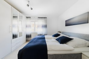 A bedroom with a bed, bedside tables, a wardrobe, and a painting on the wall. - Holiday Apartment 'Im Fischerhaus' with Private Terrace and Wi-Fi (Nonnenhorn)