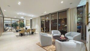 Una habitación de hotel moderna con zona de comedor, ventanas amplias y vistas a la ciudad.