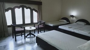 A hotel room with two single beds, a small table with chairs, and a window with decorative shutters. - Hotel Marble Palace  (Khajuraho)
