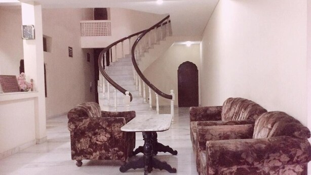 A spacious living area with a marble floor, a curved staircase, and floral-patterned sofas. - Hotel Marble Palace  (Khajuraho)