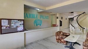 A marble reception area with a sign reading "MARBLE PALACE," a bulletin board, and a staircase. - Hotel Marble Palace  (Khajuraho)