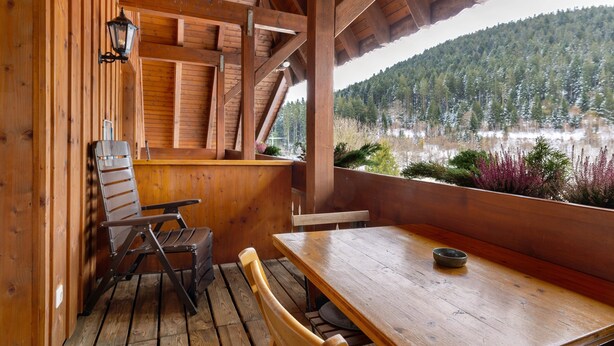 Una cabana de fusta amb taula i cadires, una banca i vista a un llac i un bosc.